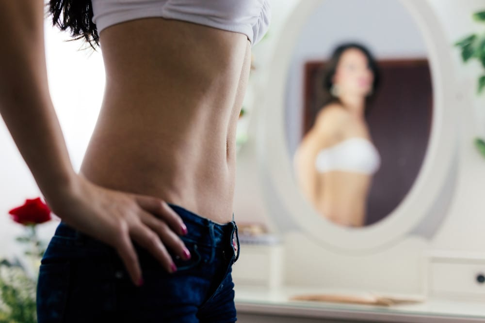 Woman looking in the mirror at her stomach.